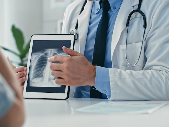 Médico sentado con su paciente y mostrando sus radiografías en una tableta digital (Getty Images)