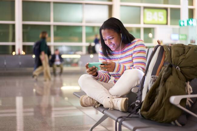 Mujer viendo películas en su celular desde el aeropuerto, mientras espera el avión.
